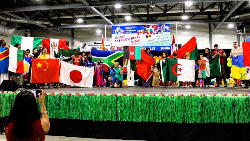 Newcomers holding the flags of their home countries on stage at the Multicultural Association’s international festival